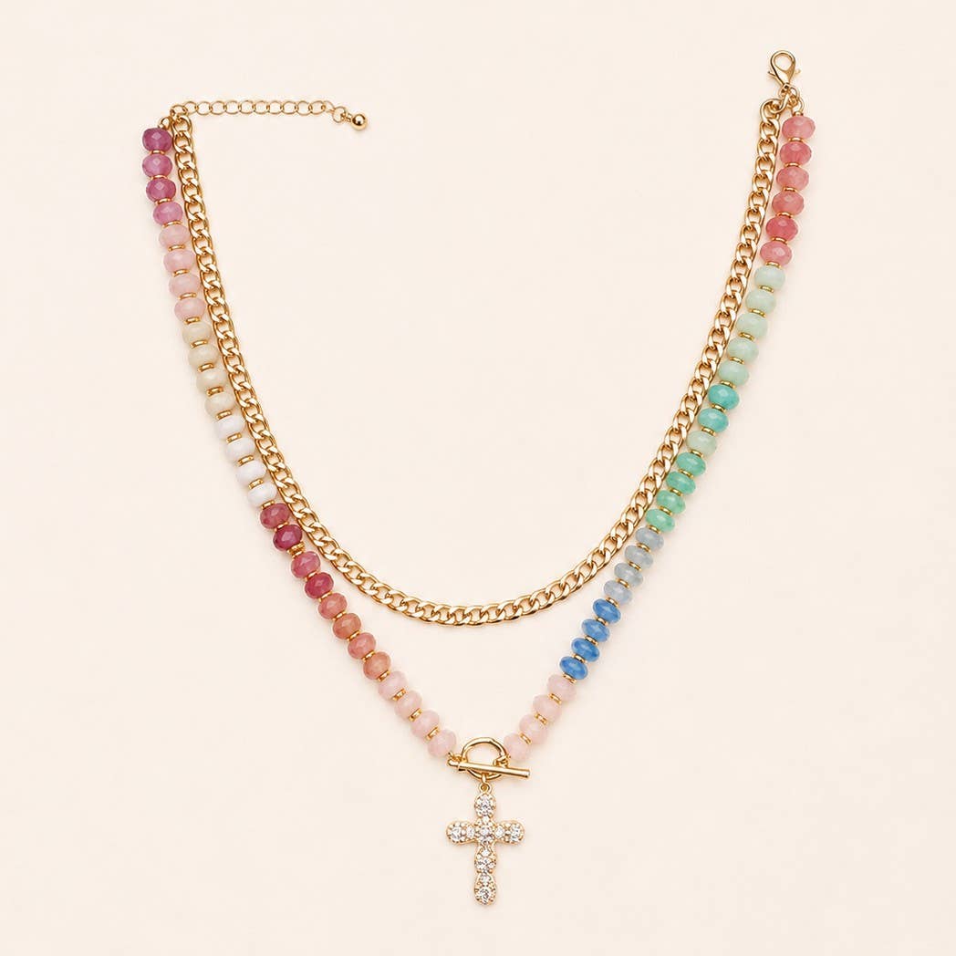 The JOSSLYN by wall to wall Multi Layer Pendant Resin Beaded Necklace features a double-strand design with one gold chain and one colorful resin bead strand, finished with a gold toggle clasp and a rhinestone-studded cross pendant.