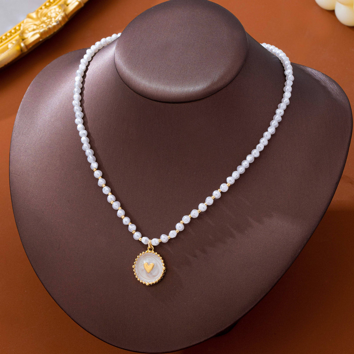 JOSSLYN by wall to wall Pearl Beaded Heart Charm Necklace featuring small white pearls accented with gold beads and a round pendant with a small gold heart.