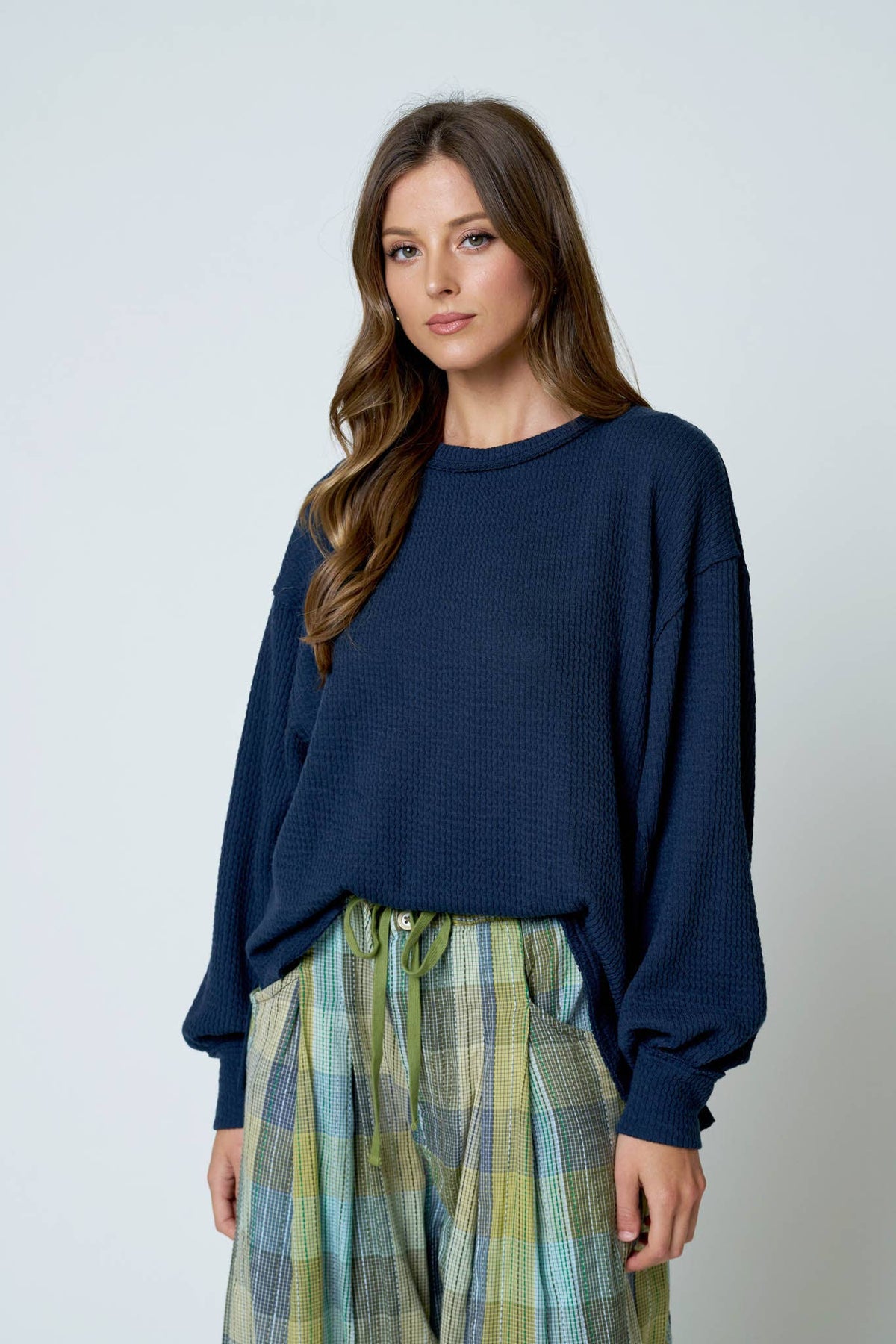 A woman wears a navy blue, long-sleeved waffle knit Navy Extended Sleeve Top by Blu Pepper featuring a crew neckline.