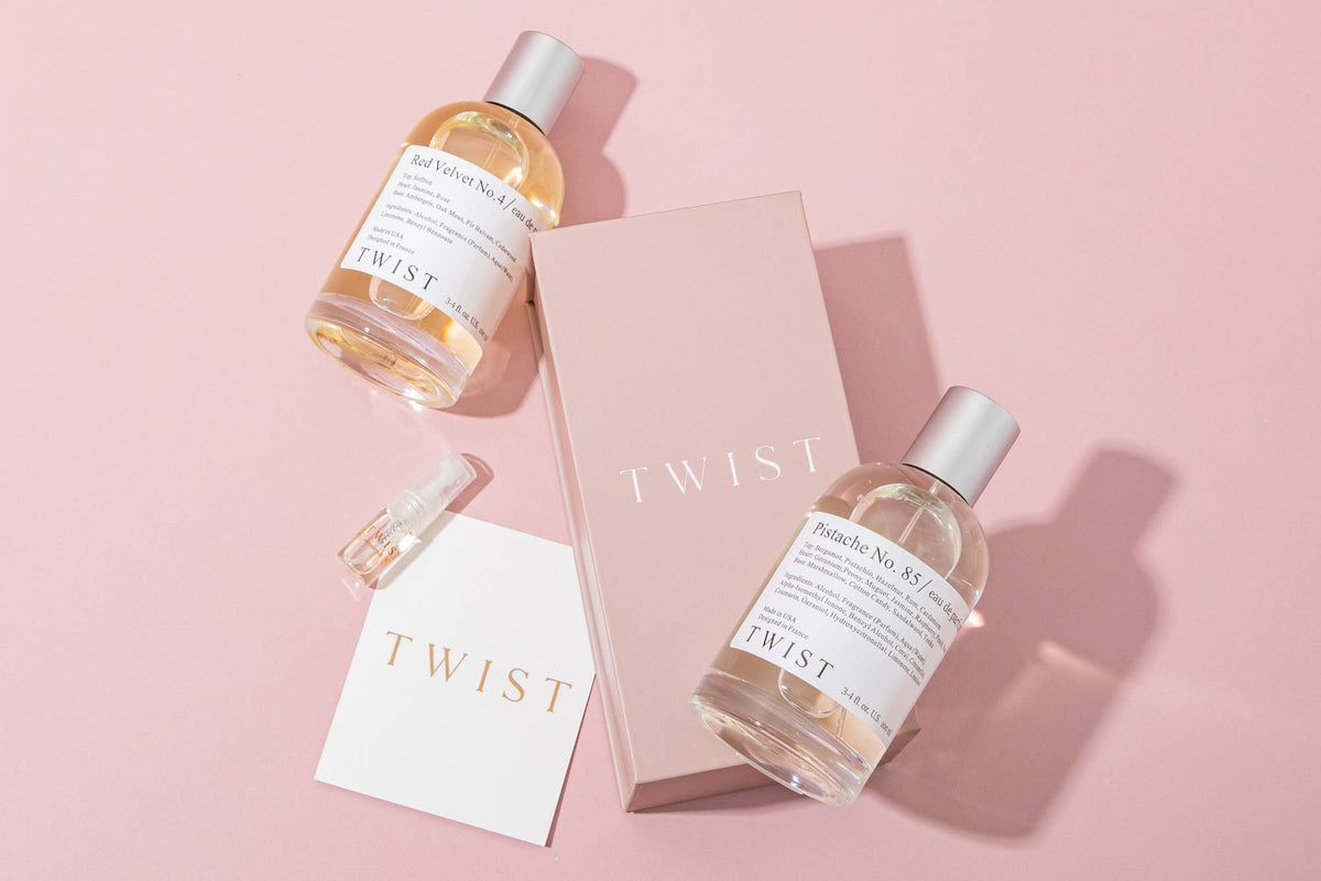 Two bottles of Sun Kissed No. 115 Perfume by House of Twist, a pink House of Twist box, a small clear spray nozzle, and a white card with gold House of Twist text, all arranged on a pink background—perfect for those seeking a long-lasting perfume with the ideal summer scent.