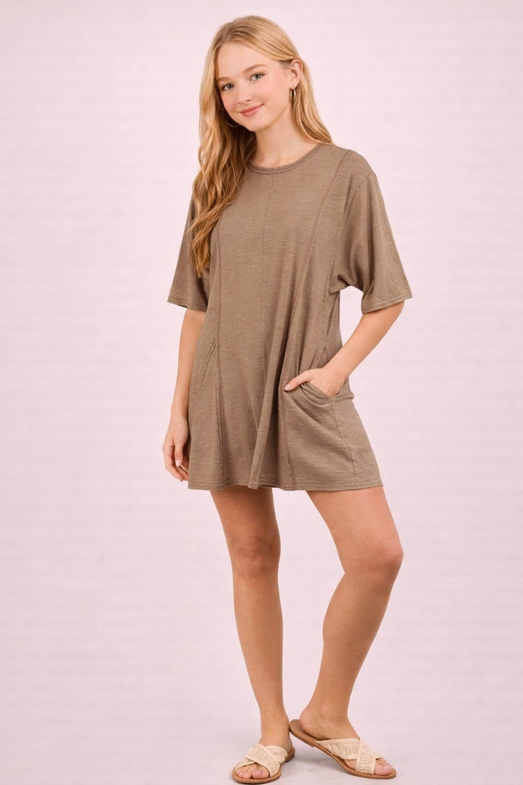 A person wears a tan Mineral Washed Oversized Romper with short sleeves, side pockets, and light-colored slide sandals.