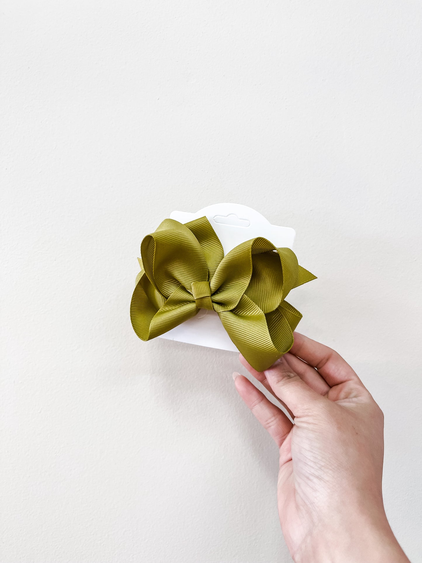A hand holds a white card showcasing the Classic Boutique Bow in olive green by funteze, set against a plain light background.