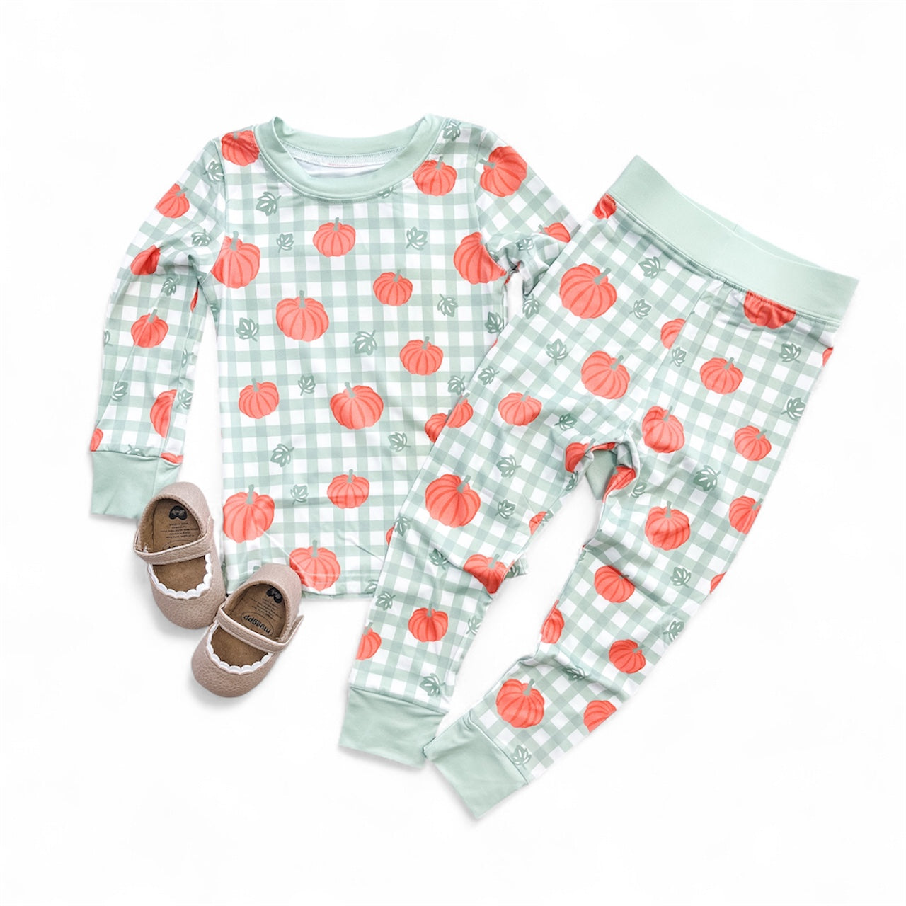 The Pumpkin Patch Long Jammies Set by Tiny Tot Bundles, featuring a mint green plaid and orange pumpkin pattern, is paired with small brown and beige moccasin-style shoes on a white background.