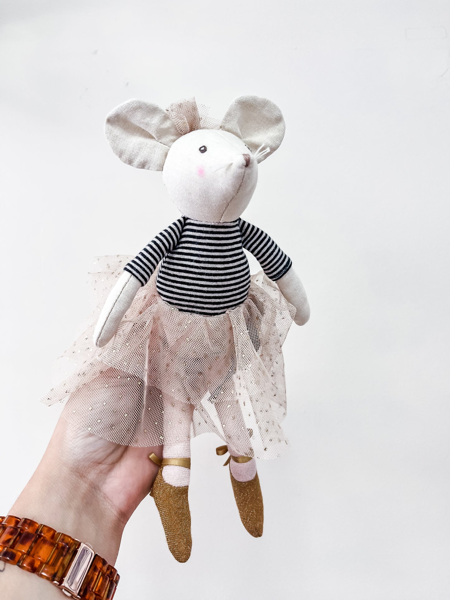 A hand wearing a brown watch holds the Little Dancer Mice Stuffed Animal by Tiny Tot Bundles, dressed in a striped shirt, pink tulle skirt, and gold shoes, against a plain white background.