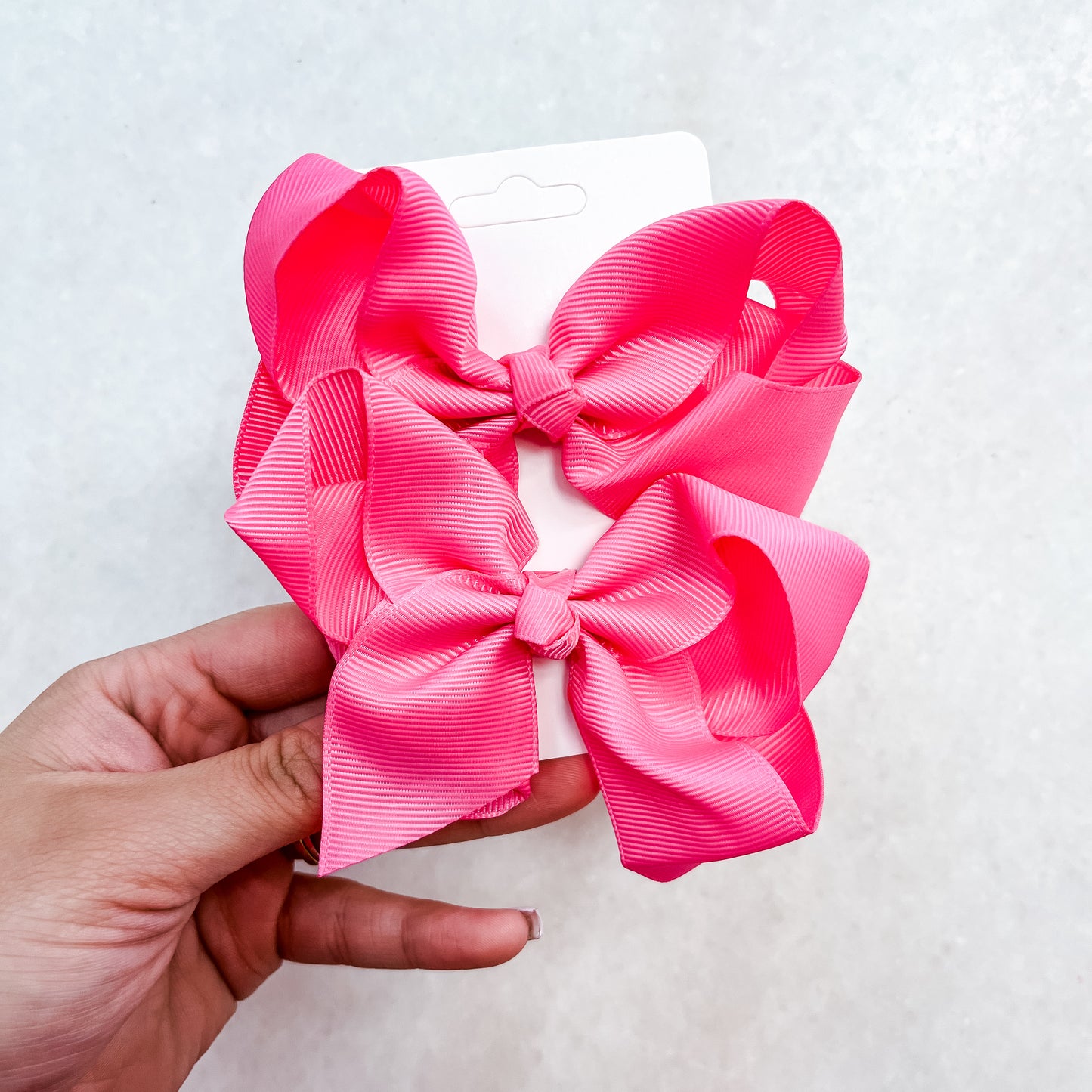 A hand displays a white card featuring two large, bright pink bows from the Pretty In Pink Bow Set by Tiny Tot Bundles, set against a light, neutral background.