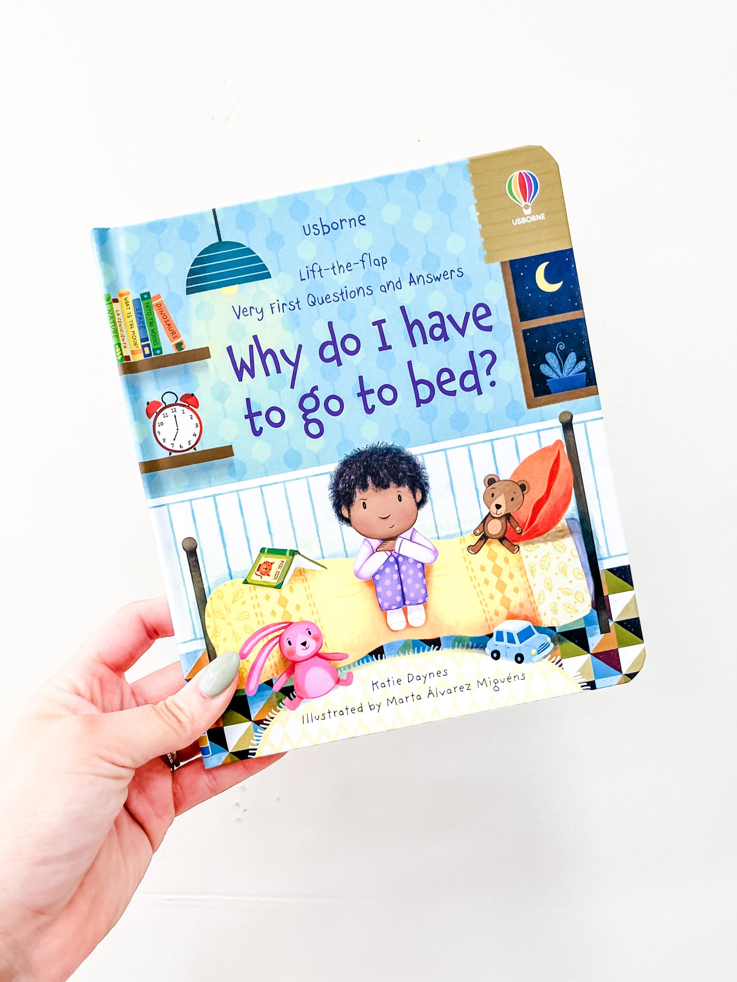 A hand holds the HarperCollins book "Why Do I Have To Go To Bed," showing a child on a bed with a teddy bear, books, and a clock in the background.