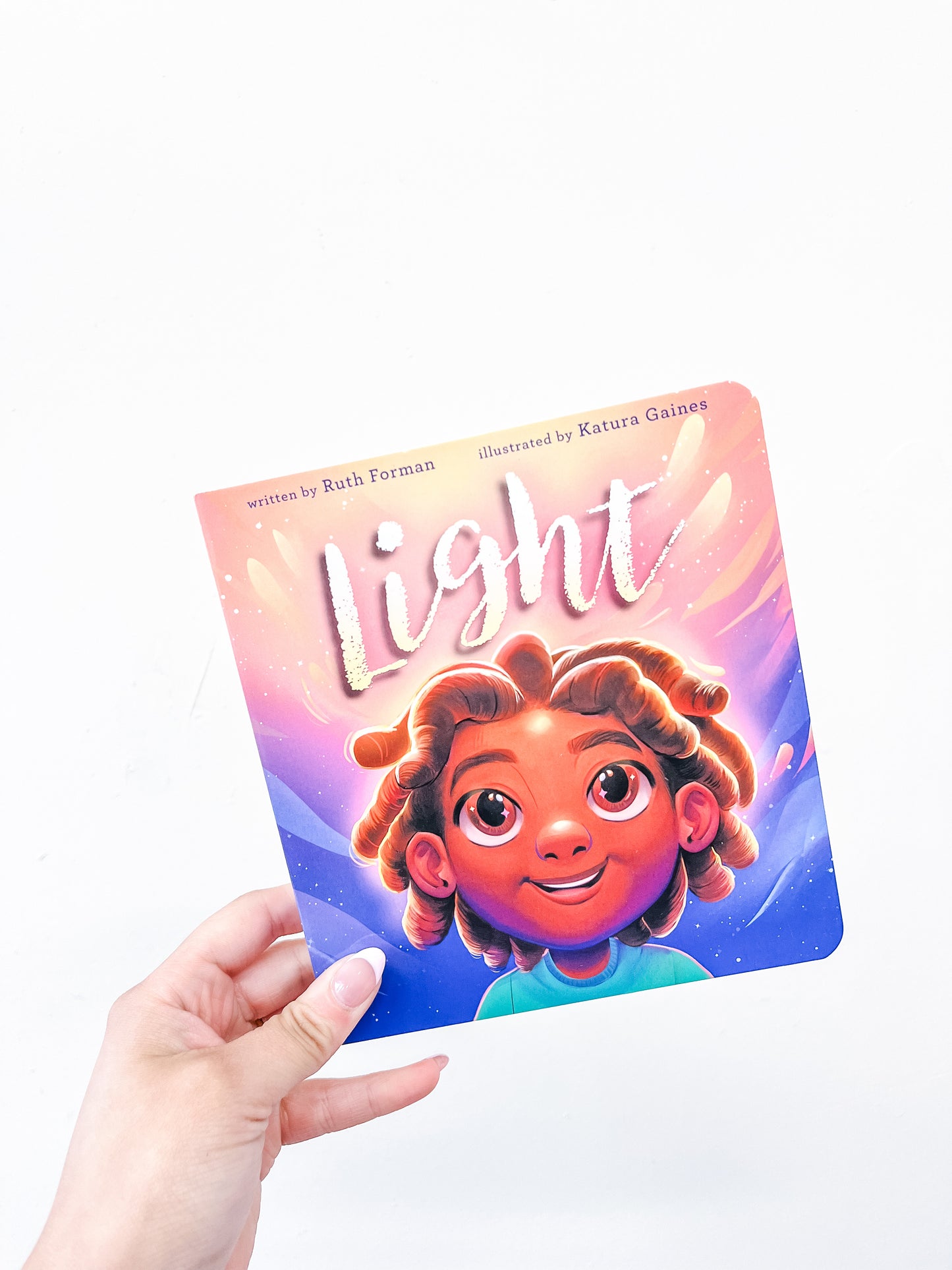 A hand holding the "Light Book" by Simon & Schuster, a children's book featuring an illustrated child with curly hair against a vibrant, glowing background.
