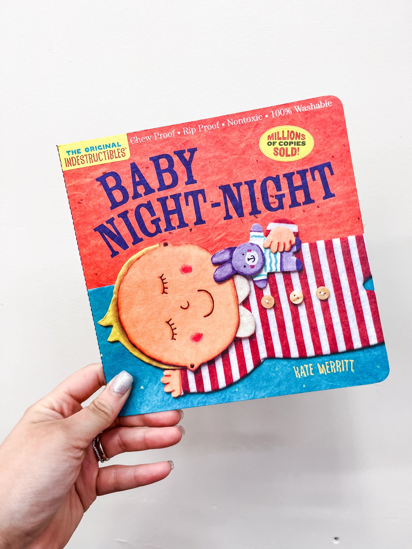 A hand holds the Baby Night, Night Book by Hachette Book Group, featuring a cover illustration of a sleeping baby hugging a purple stuffed animal.