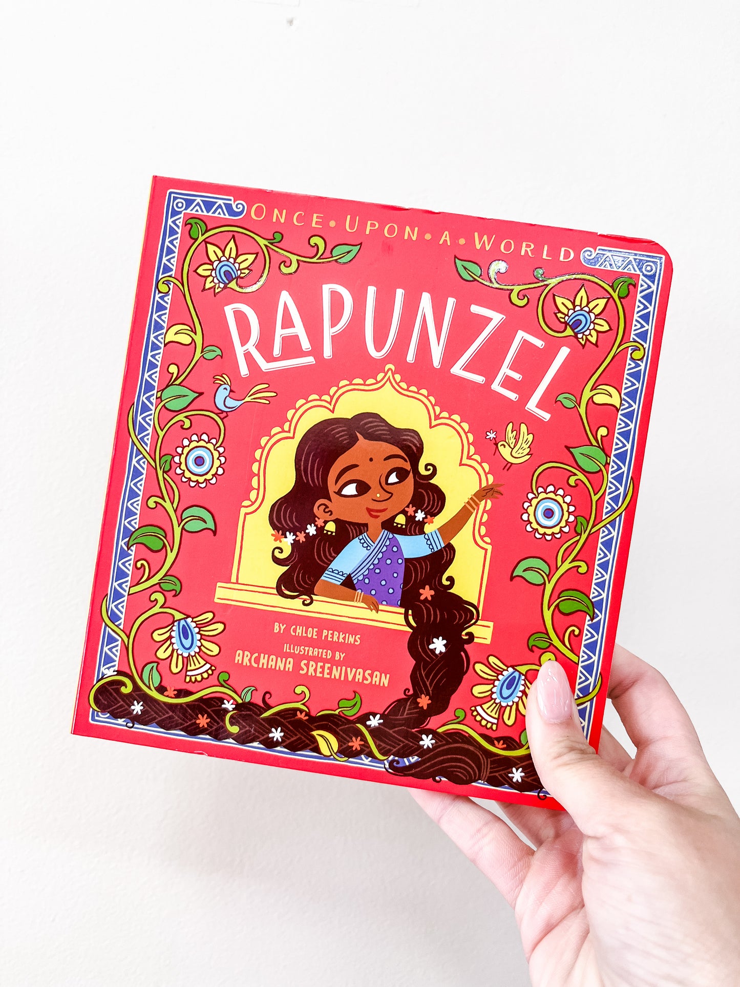 A hand holds the Rapunzel Book by Simon & Schuster, featuring an illustrated girl with long dark hair on the bright red cover.