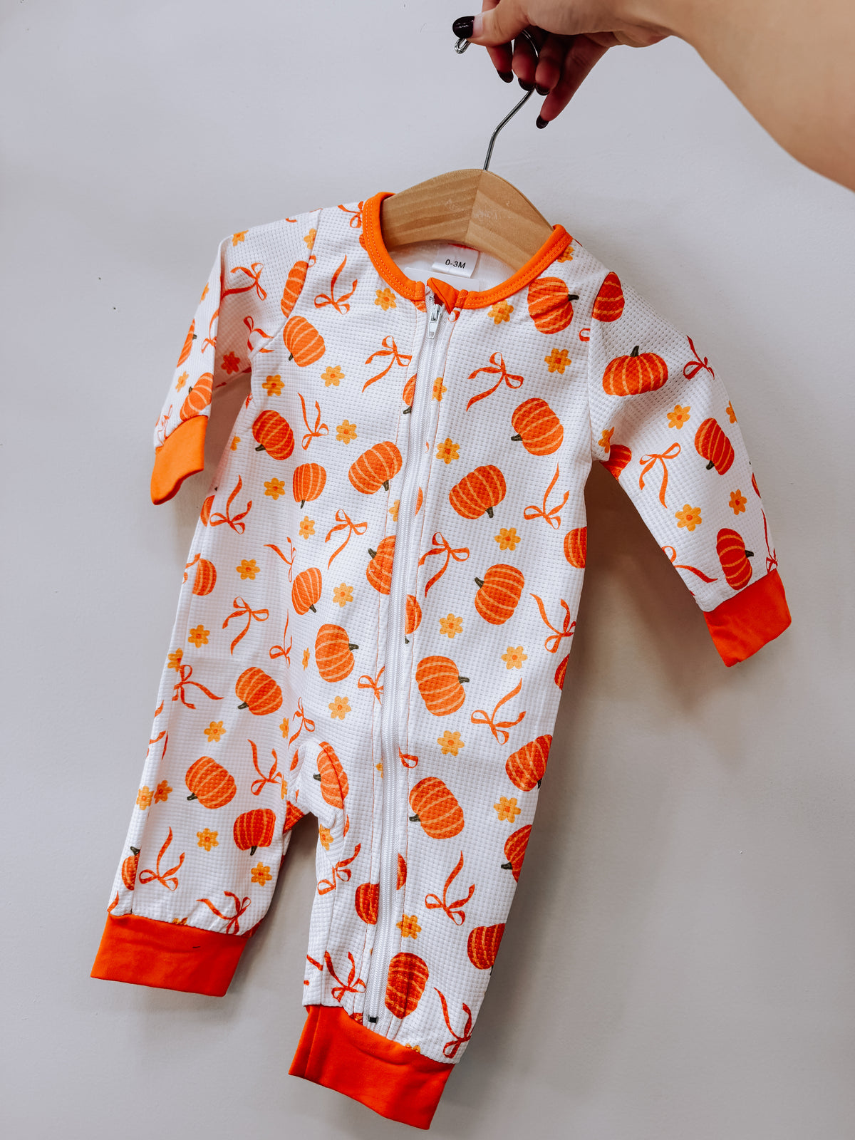 Tiny Tot Bundles Coquette Pumpkin Zippy infant long-sleeve onesie with a zipper closure, all-over print of orange pumpkins, ribbons, and small flowers, and orange cuffs.