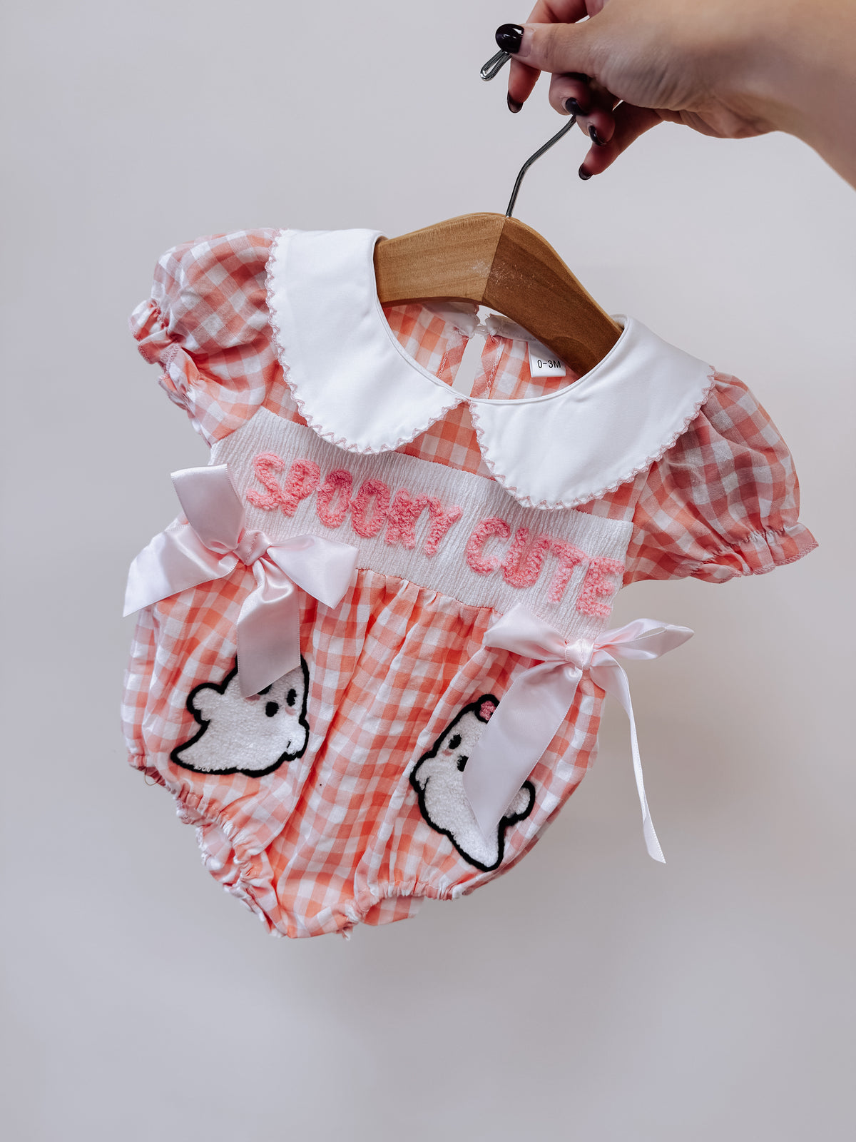 A Tiny Tot Bundles Spooky Cute Gingham Romper in pink and white with a white Peter Pan collar, SPOOKY CUTE embroidered on the chest, satin bows at the waist, and ghost appliqués.