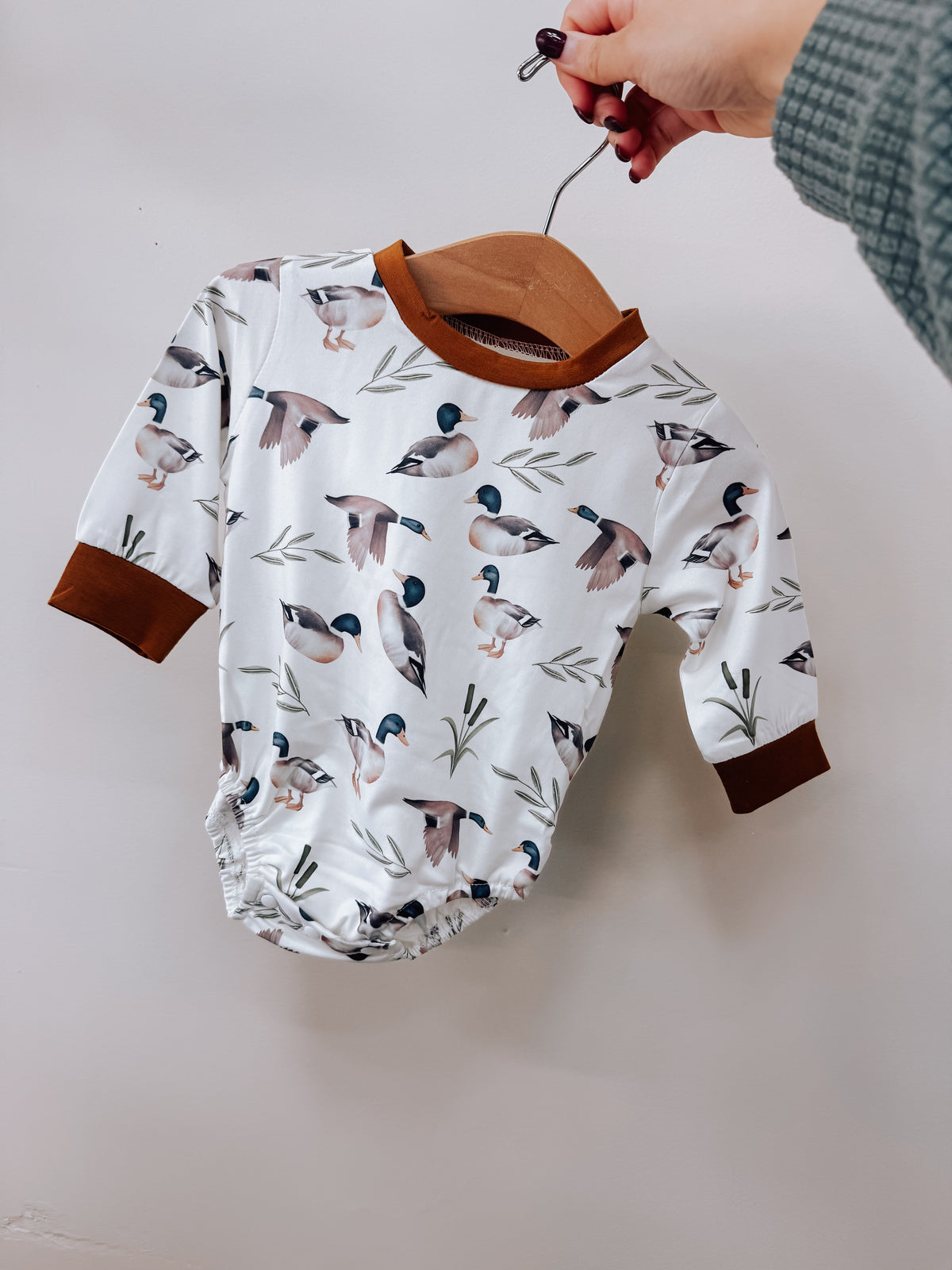 Tiny Tot Bundles Mallard Duck Ivory Romper with a mallard duck and reed print, featuring brown trim at the neckline and cuffs.