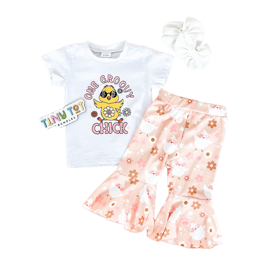 Flat lay of the Tiny Tot Bundles One Groovy Chick Bells Set: a white T-shirt with chick and “One Groovy Chick” text, peach floral flared pants, a large white hair bow, and a Tiny Tot Bundles card.