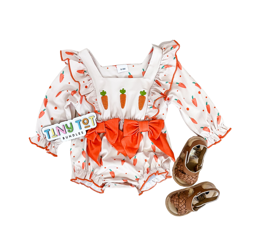 The Carrot Cozy Romper by Tiny Tot Bundles features long sleeves, carrot prints, and orange bows, paired with brown woven baby shoes and a brand tag. The set is displayed on a white background.
