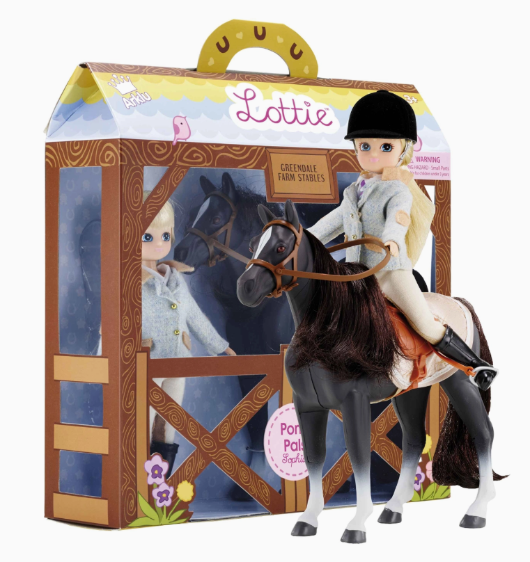 A lootie dolls Lottie Dolls - Pony Pals doll in a riding outfit and helmet sits on a black and white toy horse in front of its stable-themed packaging labeled “Lottie Dolls - Pony Pals” from lootie dolls.