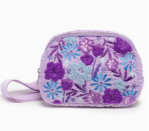 The Living Royal Lavender Bloom Belt Bag is a small, lavender zippered pouch with a wrist strap, featuring textured floral embroidery in purple and blue shades.