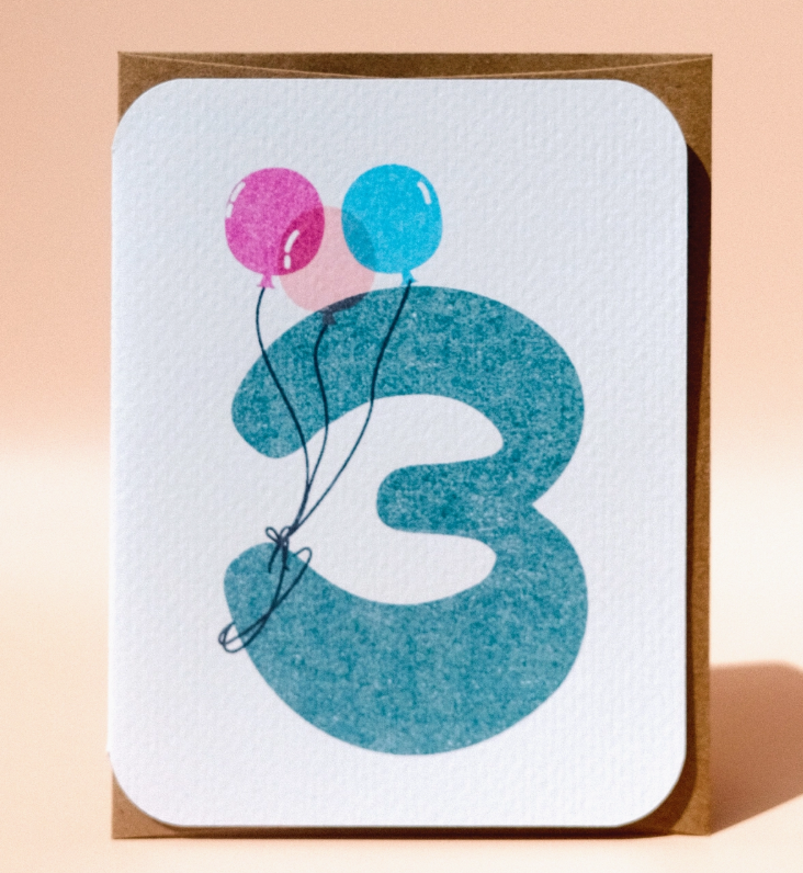 The 3rd Birthday Card by Paper Chain Studios features a large blue number 3 with pink and blue balloons attached to the top left. The card has rounded corners and a plain background.