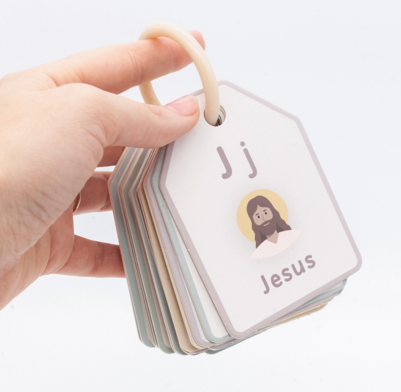 A hand holds a ring of good ground Bible ABC Flash Cards. The top card features the letter J, an illustration, and the word Jesus.