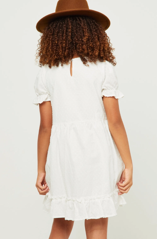 A girl with curly hair, in a brown hat and Hayden LA’s Whisper White Ruffle Dress, is shown from the back against a plain background.