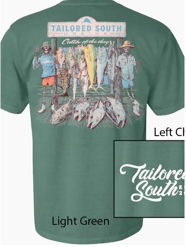 The Skeleton Fish Men T-Shirt by Wild Trail Outfitters features a light green color with a large back graphic of three people under a “Tailored South Marina” sign posing with big fish, and the “Tailored South” logo in white on the front left chest.
