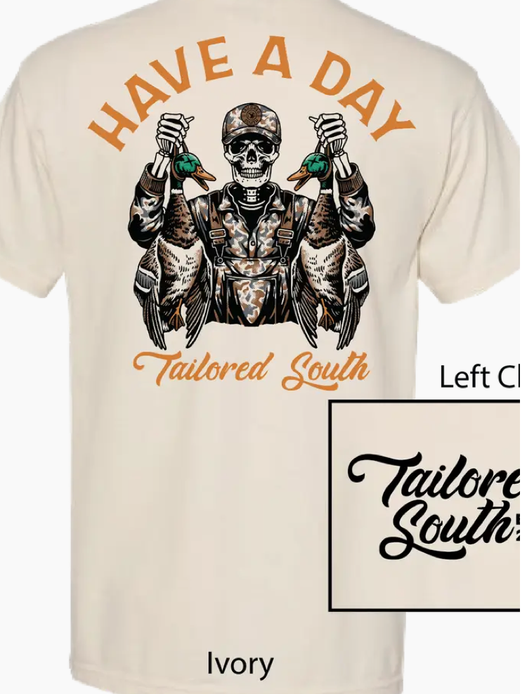 The Have A Day Ivory Men T-Shirt by Wild Trail Outfitters features a skull-faced figure in camo overalls holding two ducks, “HAVE A DAY” above, and “Tailored South” below.