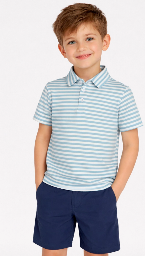 A young boy smiles in the Blue Skies Polo Set by 90 Degree by Reflex & Yogalicious, featuring a light blue and white striped polo shirt and navy shorts, with his hands in his pockets against a plain background.