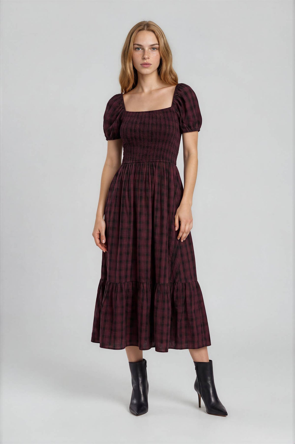 A Burgundy Plaid Midi Dress by Blu Pepper featuring a square neckline, puffed sleeves, a smocked bodice, and a tiered skirt, paired with black heeled ankle boots.