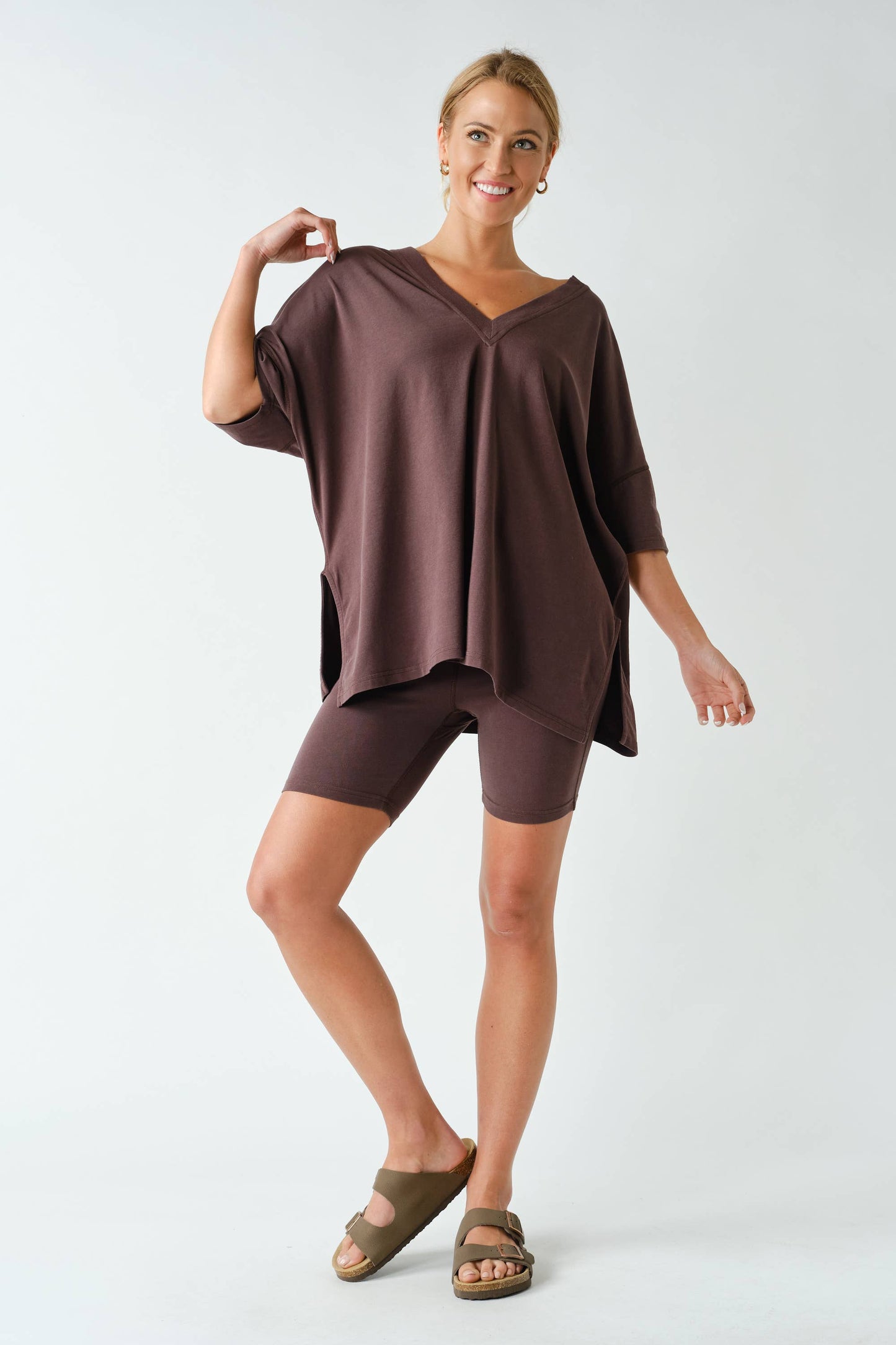 A woman stands smiling on one leg against a plain white background, dressed in the Switchback Pima Cotton Set by Mono B.
