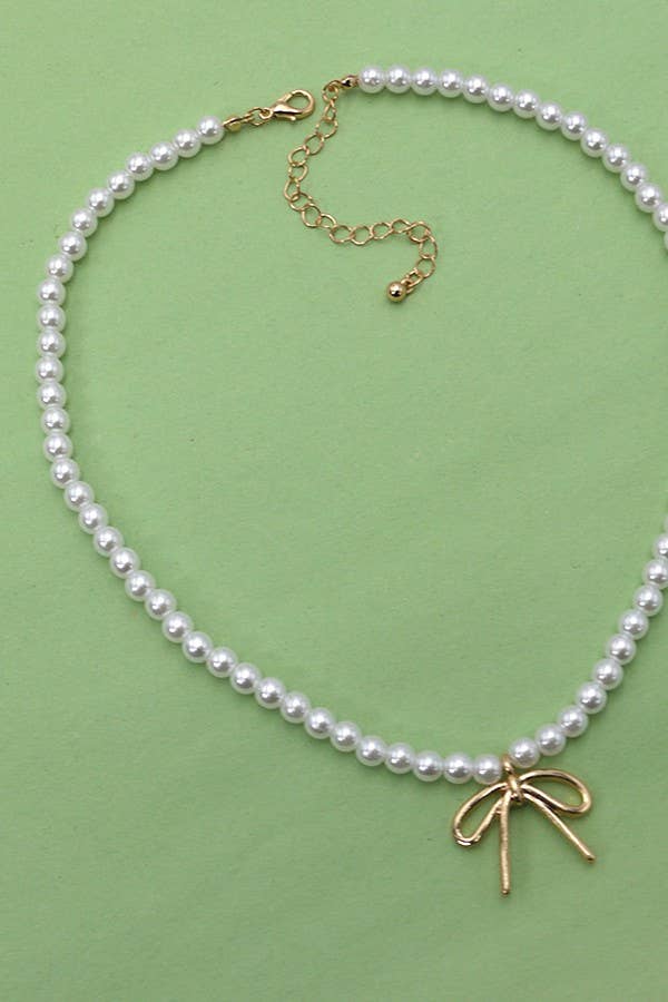 The Pearl Chain Bow Charm Necklace by JOSSLYN by wall to wall features a delicate gold bow pendant and an adjustable gold chain clasp, beautifully displayed on a light green background.