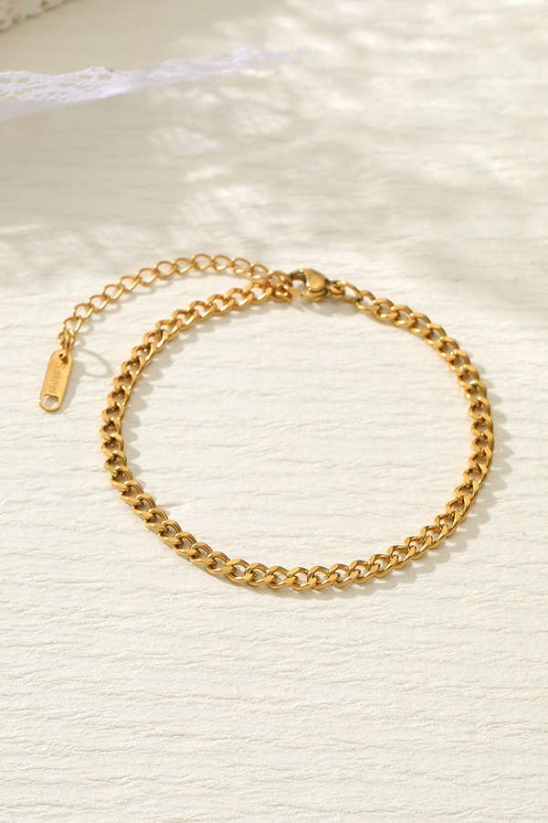 A Dainty Gold Bracelet by JOSSLYN by wall to wall, featuring an adjustable clasp and extension chain, showcased on a textured cream surface with soft natural light.