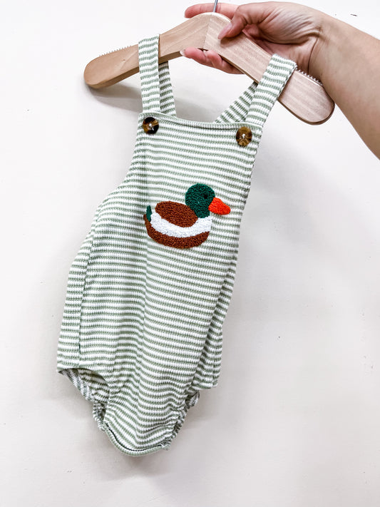 A hand displays the Tiny Tot Bundles Duck Stripe Romper—green and white stripes, wooden buttons, and a colorful embroidered duck—on a wooden hanger against a white background.