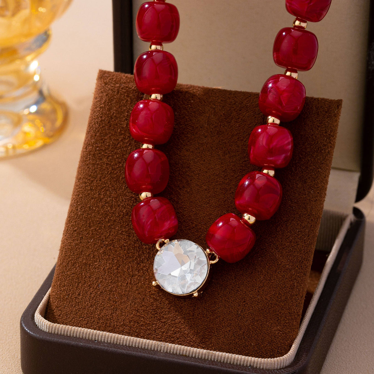A JOSSLYN by wall to wall Resin Bead Round Crystal Pendant Necklace featuring red resin beads and a round crystal pendant displayed in an open jewelry box.