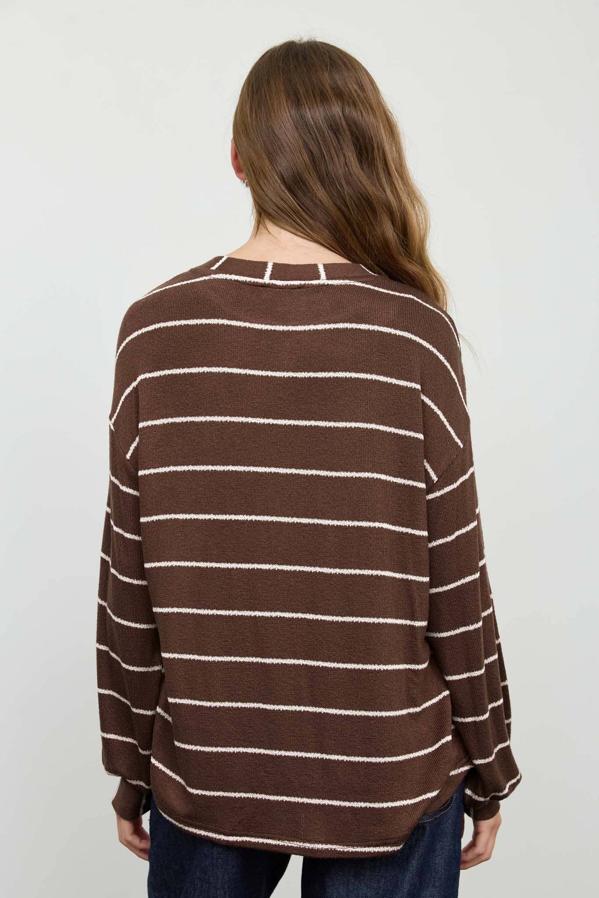 A person with long brown hair is seen from behind, wearing the Blu Pepper Brown Stripe Cuffed Knit Top and dark pants against a plain light background.