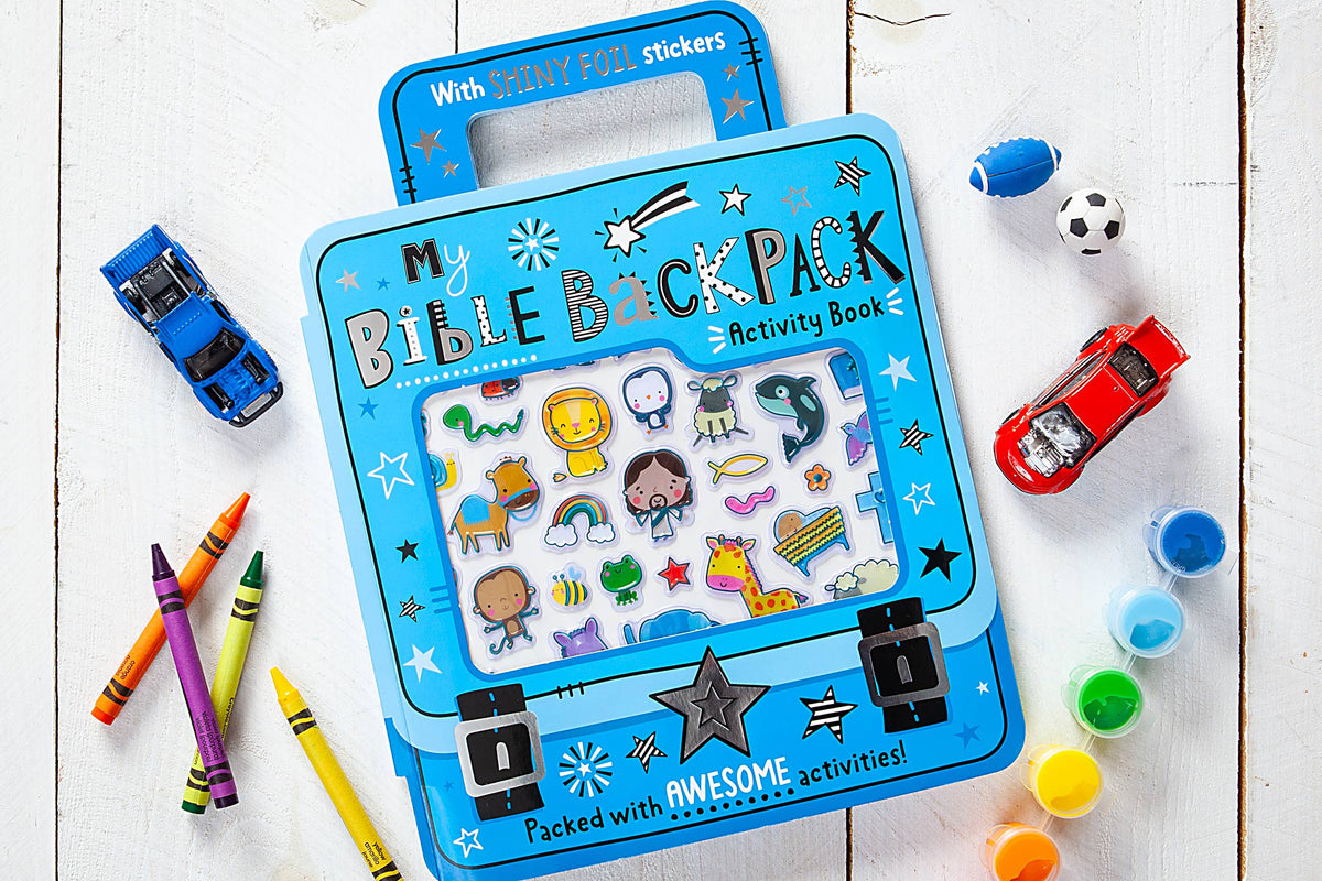 A copy of the My Bible Backpack Activity Book by BroadStreet Publishing Group, LLC in blue is displayed on a white wooden surface with animal stickers, surrounded by crayons, toy cars, a soccer ball, and a die.