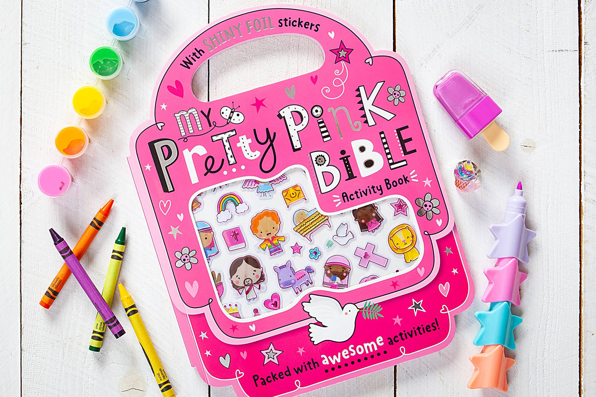 A copy of the My Pretty Pink Bible Activity Book by BroadStreet Publishing Group, LLC is displayed on a white wooden surface, surrounded by crayons, paint pots, a popsicle-shaped eraser, and stacked star-shaped erasers.