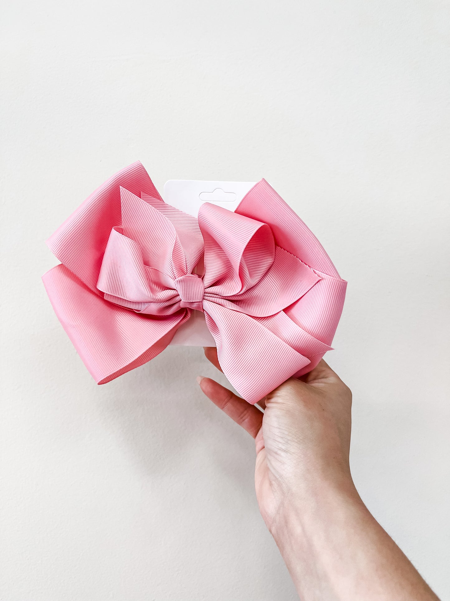 A hand holds a funteze Oversized Pastel Bow with multiple loops in pink against a plain white background.