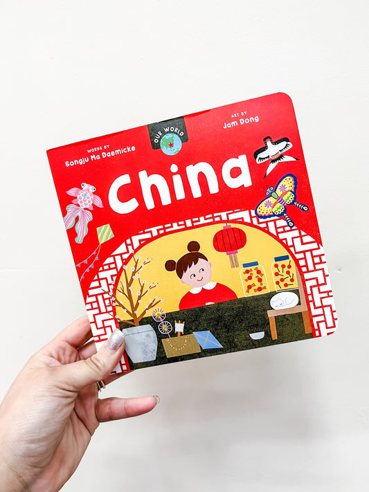 A hand holds Barefoot Books’ “Our World: China Book,” a colorful children’s board book featuring illustrations of a child, lanterns, plants, and traditional Chinese decorations on the cover.