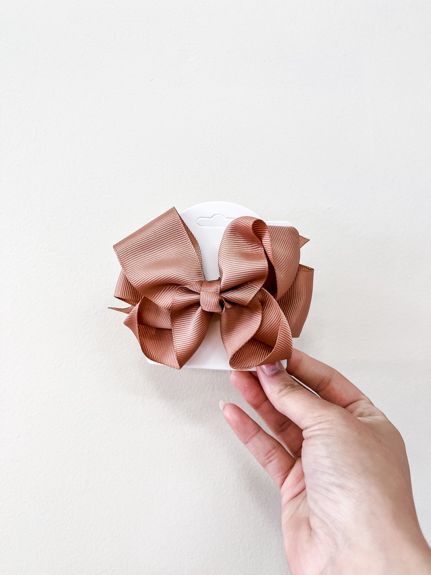 A hand holds a funteze Classic Boutique Bow, a large ribbed light brown hair accessory, displayed on a white card against a plain light background.