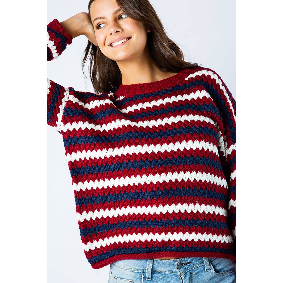 A woman smiles wearing a Sweet Generis Chunky Knit Multi Color Sweater featuring a textured, multi-colored horizontal stripe pattern in red, white, and dark blue.