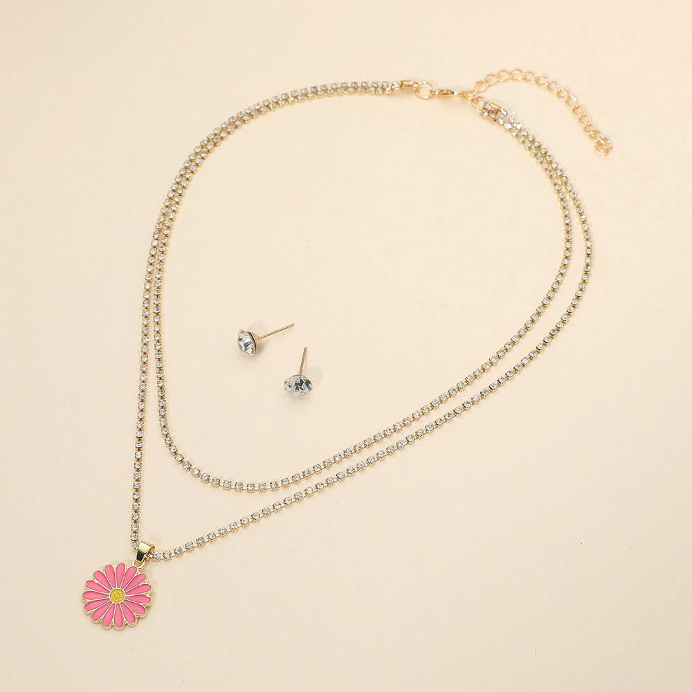 The Sensibling Corp. Flower Layered Necklaces, featuring two gold strands with a pink daisy pendant, are displayed beside simple round clear gemstone stud earrings on a light beige background.