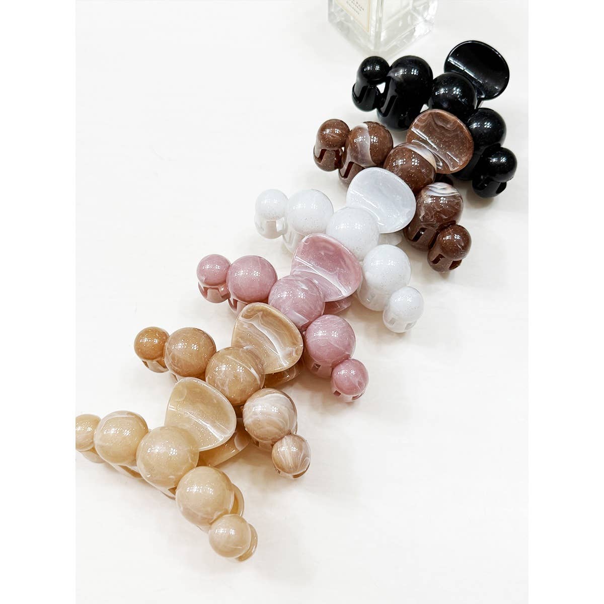 Five Love and Repeat Large Marbled Hair Claws in beige, pink, white, brown, and black are arranged in a line on a white surface. A transparent bottle is partially visible at the top of the image.