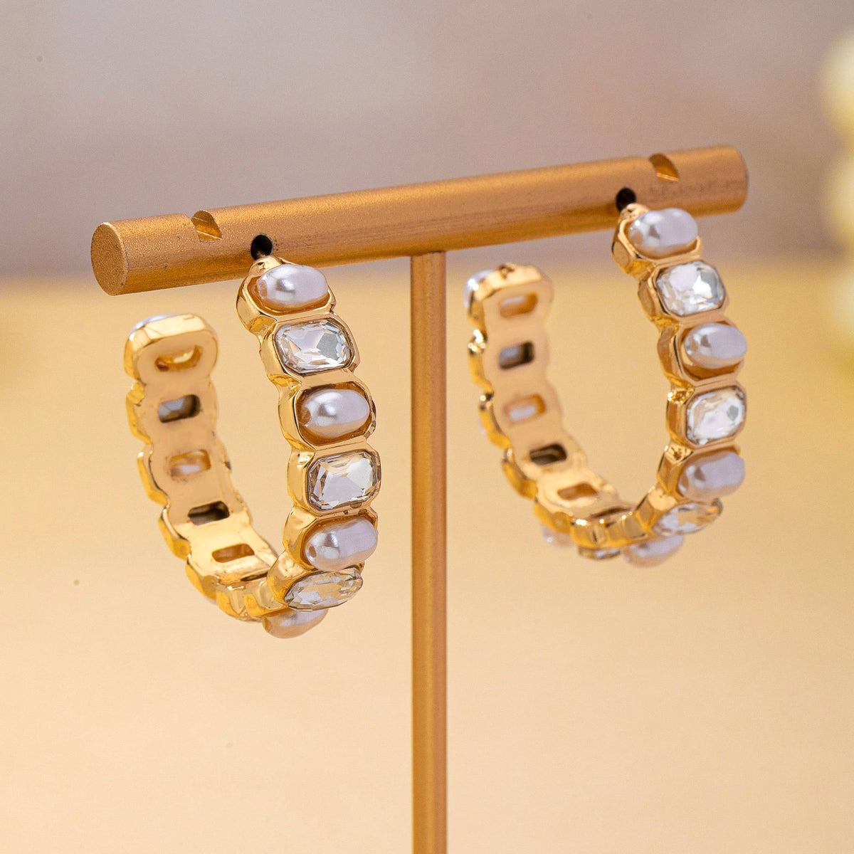 JOSSLYN by wall to wall Pearl & Rhinestone Hoop Earrings in gold featuring alternating inset pearls and clear rectangular crystals on a jewelry stand.