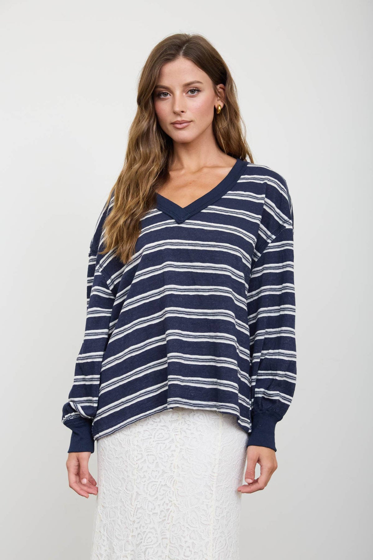 A woman wears a Blue Stripe V-Neck Long Sleeve navy blue top with white horizontal stripes.