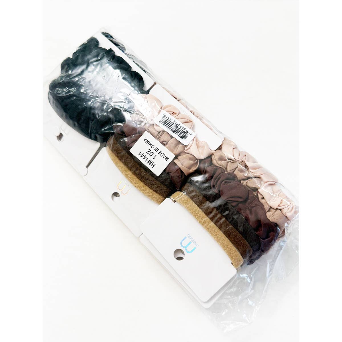 A clear plastic bag from Love and Repeat contains an Assorted Hair Tie & Scrunchie Set, featuring multiple sets of fabric scrunchies in various colors—black, beige, pink, brown, and gold—each displayed on a white card.