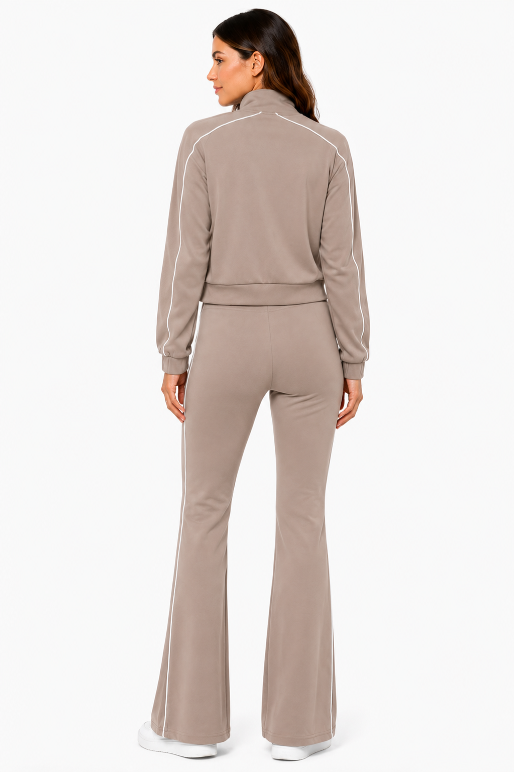 A woman stands facing away against a white background, dressed in the Color 5 Mocha Muse 3-Piece Athletic Set—a taupe velour tracksuit with white piping, flared pants, and paired with white sneakers.