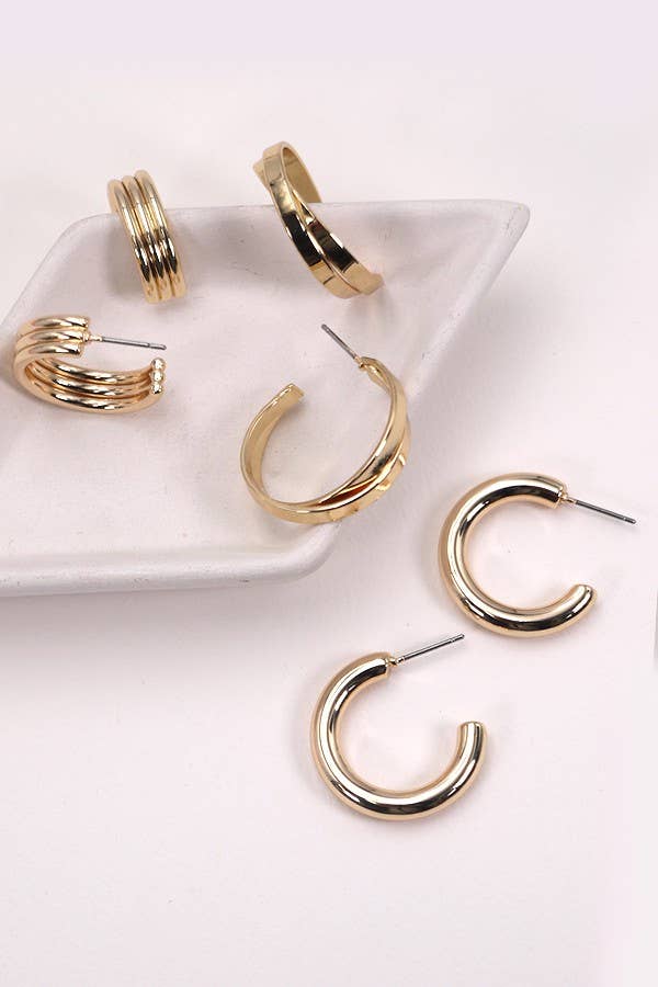 Displayed on and beside a white, triangular ceramic dish against a light background, the JOSSLYN by wall to wall Multi Hoop Trio Earring Set showcases three pairs of gold hoops in varying thicknesses.