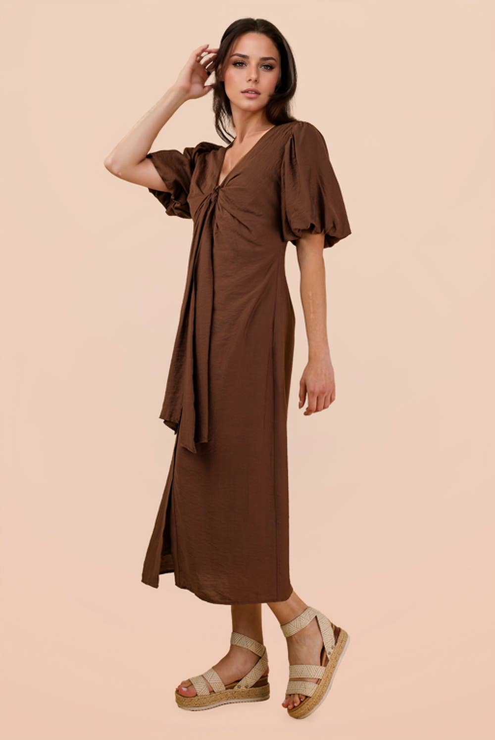 A woman wears a brown VERY J Mocha Front Tie Midi Dress with a V-neck, puff sleeves, and a knotted front, paired with tan platform espadrille sandals.