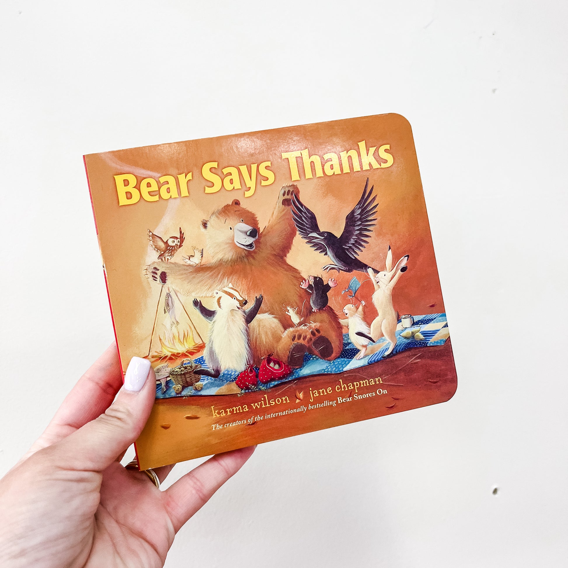 A hand holds the Bear Says Thanks Book by Simon & Schuster, featuring illustrated animals joyfully gathered around a meal on the cover.