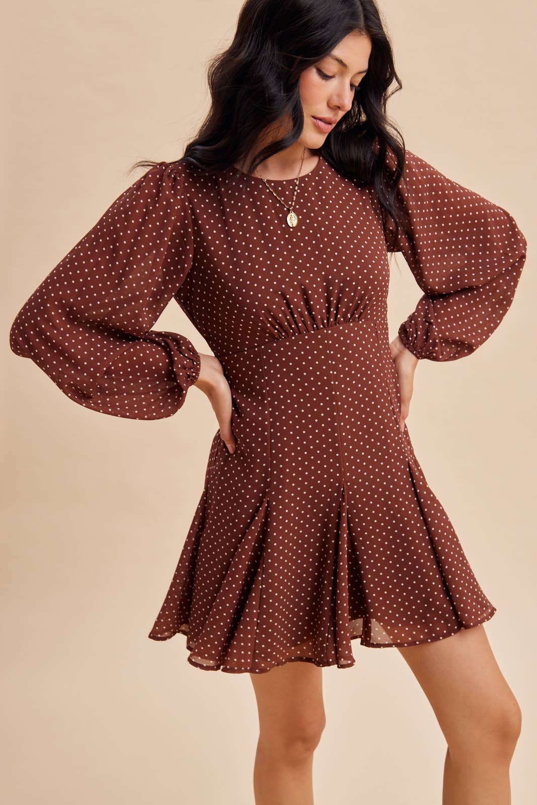 In Loom Polka Dot Flared Mini Dress in brown with white polka dots, long blouson sleeves, and a flared pleated skirt.
