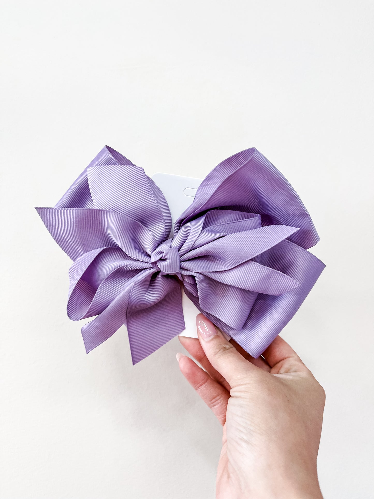 A hand displays an Oversized Pastel Bow in lavender by funteze, featuring a textured design against a plain white background.